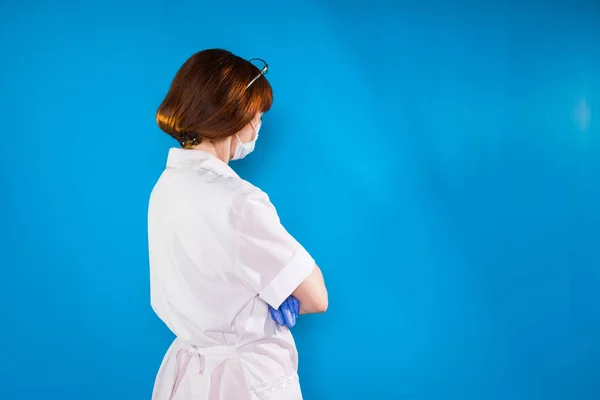 Roodharige vrouw arts in witte medische robe staat met terug naar de camera — Stockfoto
