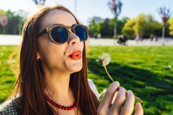 Divertente sorridente donna felice in occhiali da sole che soffia dente di leone — Foto Stock