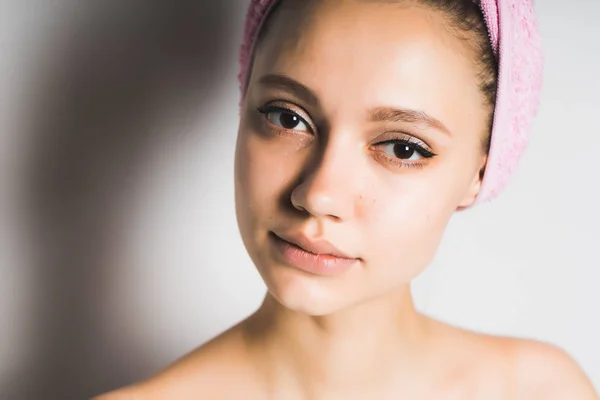 Jovem menina bonita com pele limpa olha para a câmera, na cabeça uma toalha rosa — Fotografia de Stock