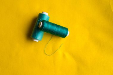 Sarı bir arka plan üzerinde renkli iplik bobinleri vardır