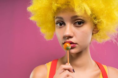 güzel genç kız ile sarı palyaço peruk başında chupa chups elinde tutar.