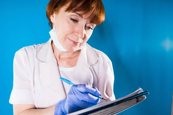 Adulto esperto medico femminile in bianco medicazione medica scrive in schede paziente — Foto Stock