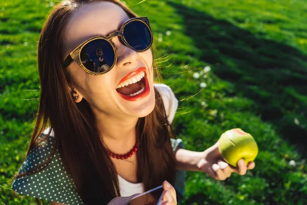 Счастливая смеющаяся женщина, открытый рот, сидит на зеленой траве в парке — стоковое фото
