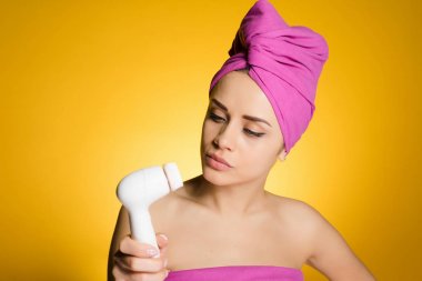 Kafasındaki bir pembe havlu ile genç kız olun deri elektrikli bir fırça ile yüzünde derin bir temizlik