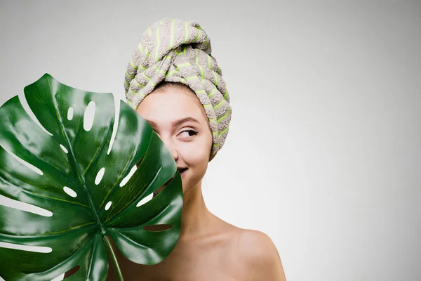 Niña sonriente con una toalla en la cabeza, cubriéndose la cara con una hoja verde — Foto de Stock