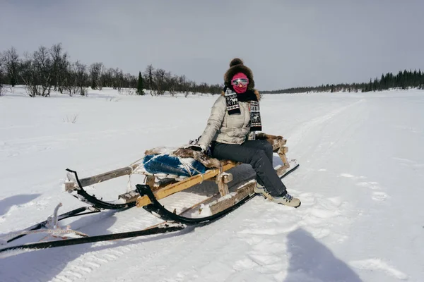 Ein Mädchen in warmer Kleidung und Pelzmütze reist nach Norden, sitzt auf einem Schlitten, um weißen Schnee — Stockfoto