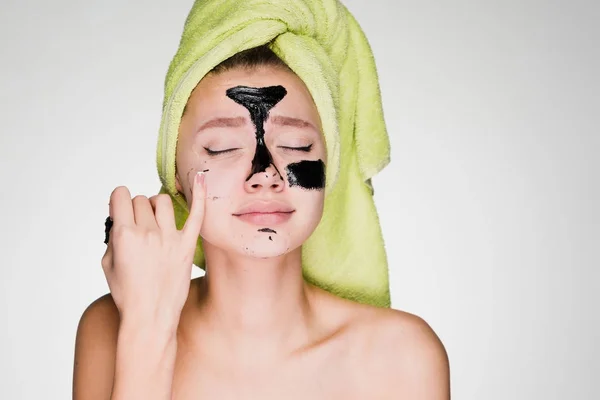 A young girl with a green towel on her head puts on her face a black mask against black dots — Stock Photo, Image