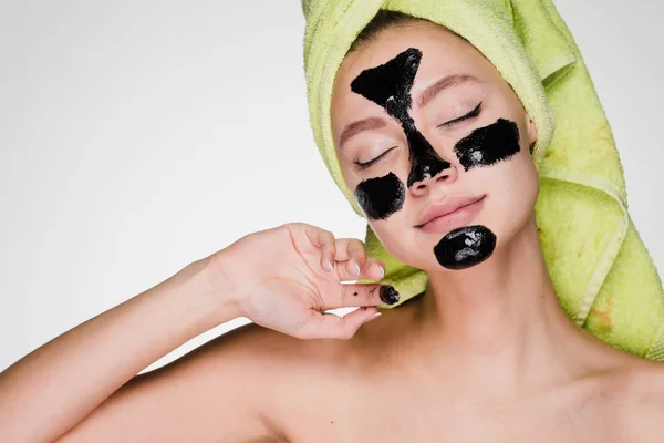 Hermosa chica con una toalla verde en la cabeza hace un tratamiento de spa, n cara una máscara de limpieza negro — Foto de Stock