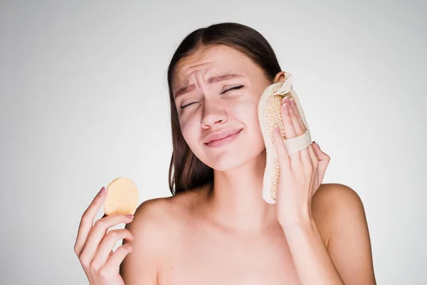 Unzufriedene junge Mädchen reinigen die Gesichtshaut mit einem speziellen Schwamm — Stockfoto
