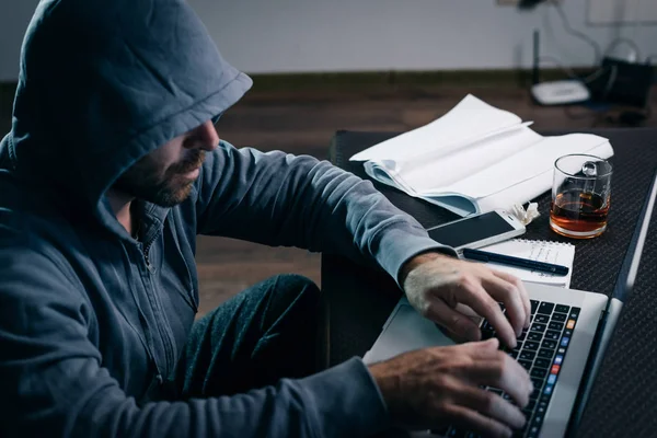 a mysterious man in a hood illegally hacks something through a computer