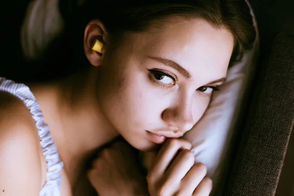 美しい少女はベッドの上にある、黄色の耳栓は騒音に対して耳で寝たいです。 — ストック写真