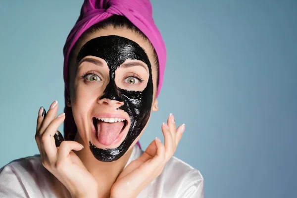 En rolig vacker flicka med en rosa handduk på huvudet tillämpas en svart cleansing mask på ansiktet — Stockfoto