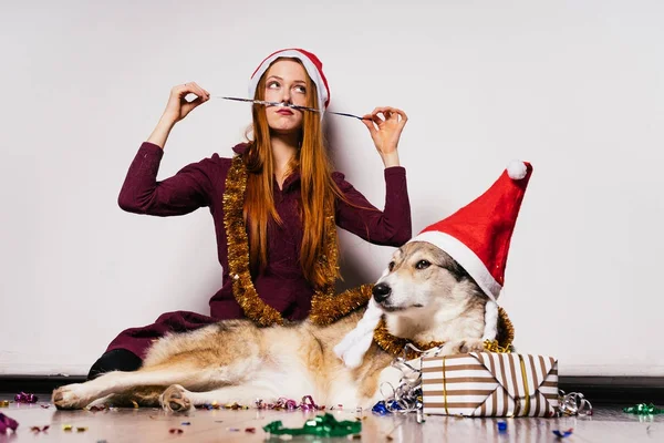 Руда красива дівчина сидить на підлозі зі своєю собакою, чекаючи Нового року, багато яскравої мішури — стокове фото