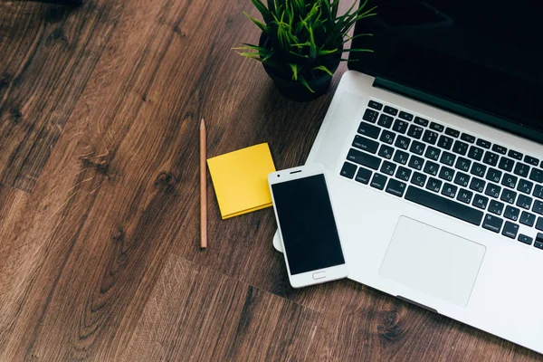 Sobre un fondo de madera hay un ordenador portátil, un smartphone para el trabajo, un papel y un lápiz — Foto de Stock