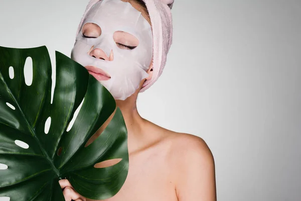 beautiful girl arranged a day spa, on the face a tissue mask, holds a green leaf