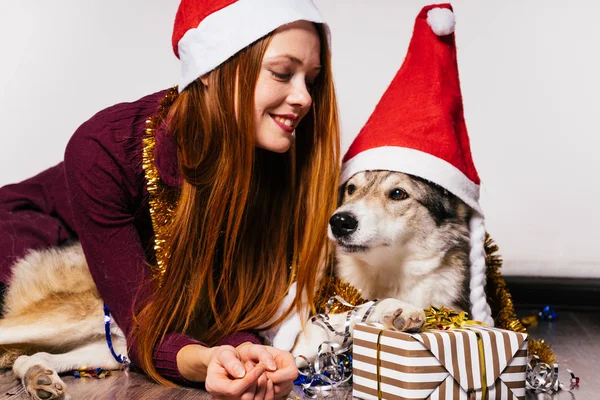 彼女の犬は、多く明るい見掛け倒しの新年を祝う赤い帽子に赤い髪の少女に笑みを浮かべて — ストック写真