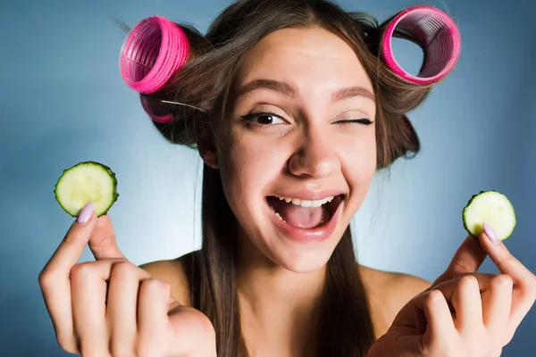 Se smíchem krásná dívka chce vypadat dobře, na hlavě kulma, udržuje kousky okurky pro hydrataci pokožky — Stock fotografie