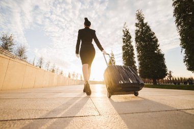 Bir kadın uçuş görevlisi bavulla üniformalı bir uçuş, güneş ışınlarının devam ediyor