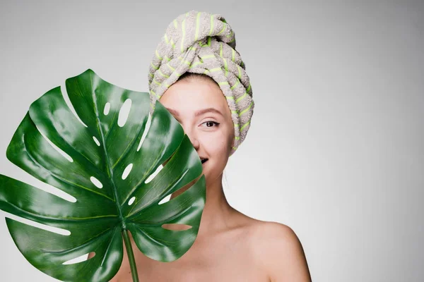 Hermosa chica con una toalla en la cabeza en el spa, escondido con una gran hoja verde — Foto de Stock