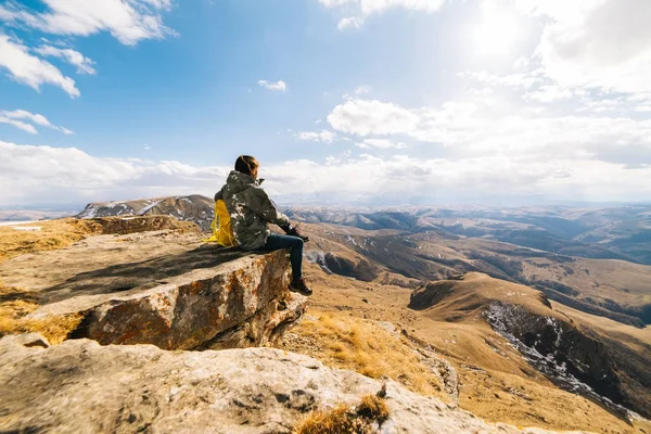 Жінка-мандрівник сидить на краю скелі, дивиться на гори, насолоджується чистим повітрям і сонцем — стокове фото