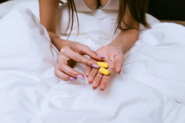Dívka sedí v posteli pod bílou přikrývkou, drží žluté špunty do uší proti hluk z ulice — Stock fotografie