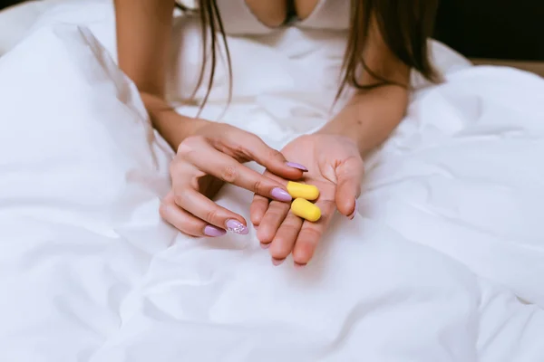 Fille assise dans le lit sous une couverture blanche, tenant bouchons d'oreilles jaunes contre le bruit de la rue — Photo