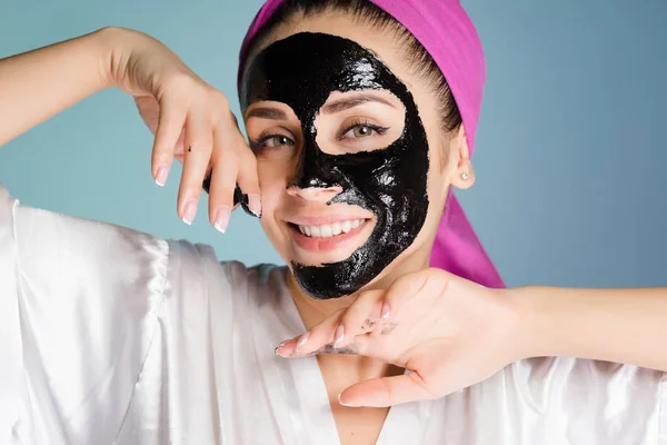 Uma menina sorrindo quer ter a pele limpa, aplicou uma máscara de limpeza preta — Fotografia de Stock