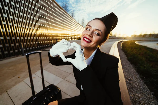 Šťastná dívka krásná letuška s úsměvem, miluje svou práci a rovin, dělá její srdce s rukama — Stock fotografie