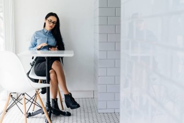 dalgın genç kız öğrenci bir mavi gömlek ve gözlük bir kafede oturan ve Üniversitesi'nde dersler sonra bir tablete yazma