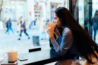 genç esmer kız öğrencinin üniversitede dersten sonra bir kafede sıcak kahve içer ve pencereden görünüyor