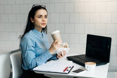 güzel genç esmer kız bir sandviç ve kahve, iş için bir dizüstü bilgisayar masası ile bir kafede Öğle Yemeği