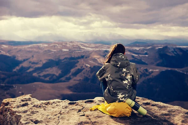 La chica se sienta en el borde de la roca, disfruta de las montañas y la naturaleza, medita —  Fotos de Stock