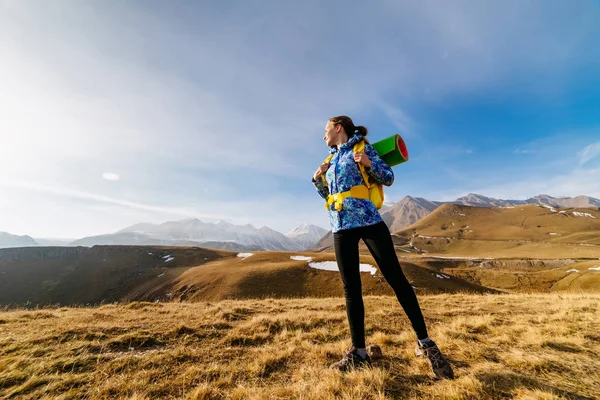 Активная спортивная девушка в синей куртке путешествует по Кавказским горам с рюкзаком и палаткой — стоковое фото