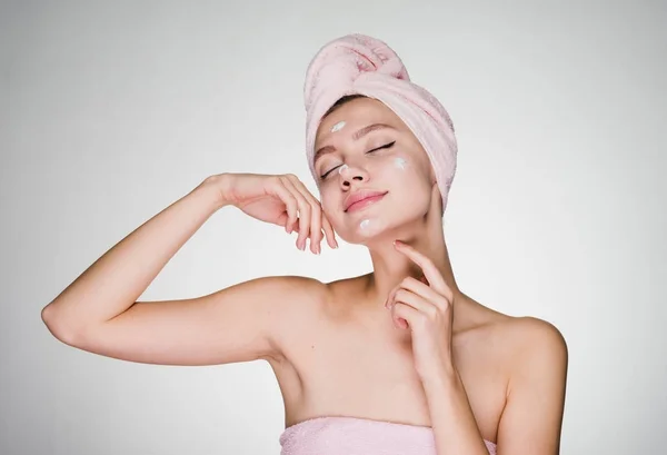Attractive young girl with a pink towel on her head applies a useful face cream — Stock Photo, Image