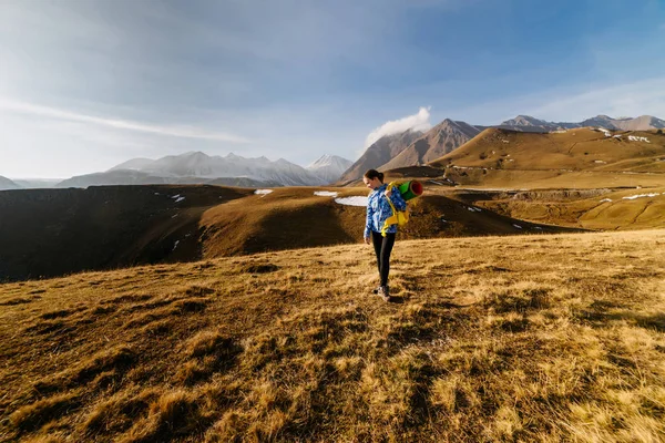 Una giovane ragazza con una giacca blu conduce uno stile di vita attivo, viaggia lungo la cresta caucasica con uno zaino — Foto Stock