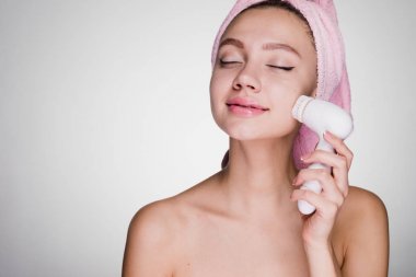 Elektrik fırça ile fırçalama yüz yapıyor başında bir havlu ile çekici mutlu kız