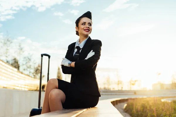 Boldog, mosolygós nő stewardess egységes bőrönddel neki járatra vár — Stock Fotó