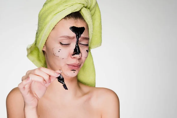 Divertida joven con una toalla verde en la cabeza quita una máscara negra de su cara — Foto de Stock