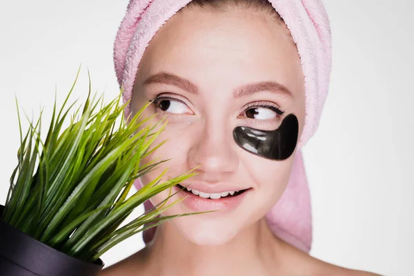 Souriant belle fille avec une serviette sur la tête, sous les yeux de taches noires, tient dans sa main un pot d'herbe — Photo