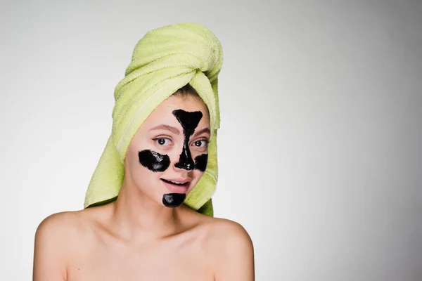 Une jolie jeune fille avec une serviette verte sur la tête a appliqué un masque nettoyant noir sur les zones problématiques sur son visage — Photo