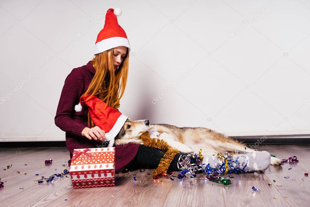 red-haired girl sits on the floor with her dog, waiting for the new year 2018, a lot of tinsel and a gift