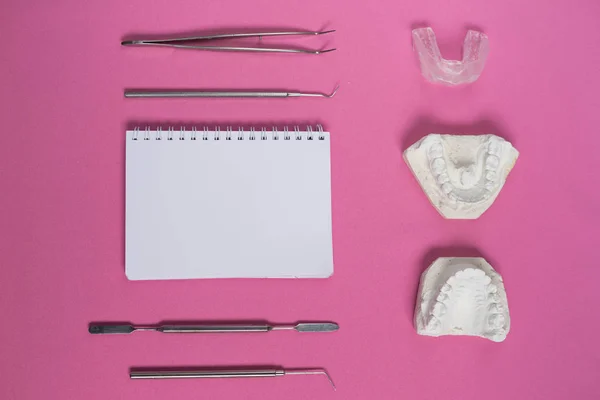 En la superficie rosa es un yeso de dientes, instrumentos dentales y un cuaderno — Foto de Stock