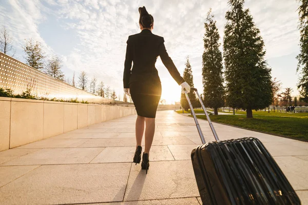 Una giovane donna snella di una hostess in uniforme con una valigia va in volo — Foto Stock