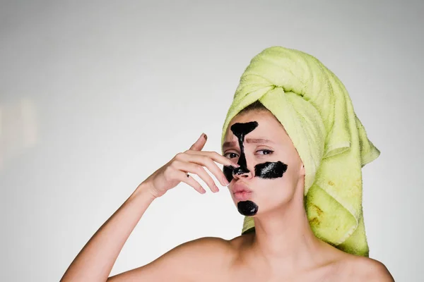 Een jong meisje met een groene handdoek op haar hoofd toegepast een zwart masker om de probleemgebieden te reinigen — Stockfoto