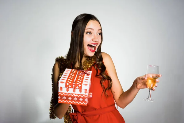 Смеющаяся счастливая девушка в красном платье, празднующая Новый 2018 год, держа в руках бокал шампанского и подарок — стоковое фото