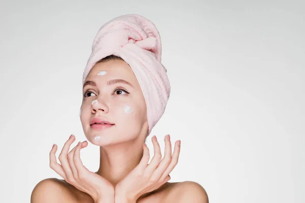 Красивая молодая девушка с розовым полотенцем на голове нанесла питательный крем на лицо — стоковое фото