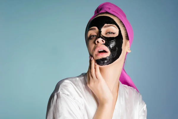 Jolie jeune fille avec une serviette rose sur la tête, sur son visage un masque nettoyant noir — Photo