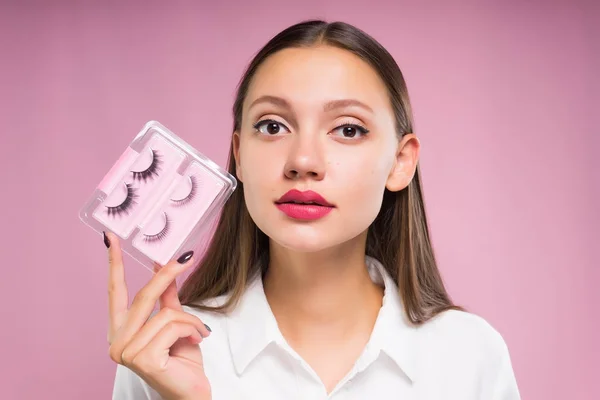 Junges Mädchen mit einem Satz falscher Wimpern auf rosa Hintergrund — Stockfoto
