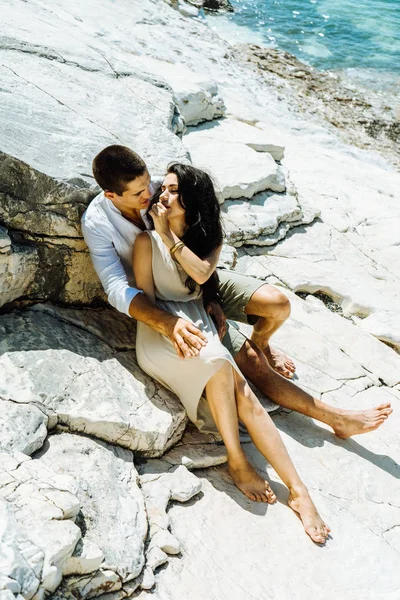 Aşık bir çifti kayaların üzerinde oturur ve deniz arka planı kisses — Stok fotoğraf