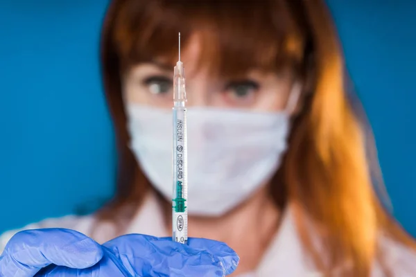 Médico adulto femenino se prepara para usar la jeringa sobre fondo azul — Foto de Stock